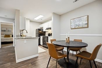 A dining area with a table and chairs and a kitchen in the background